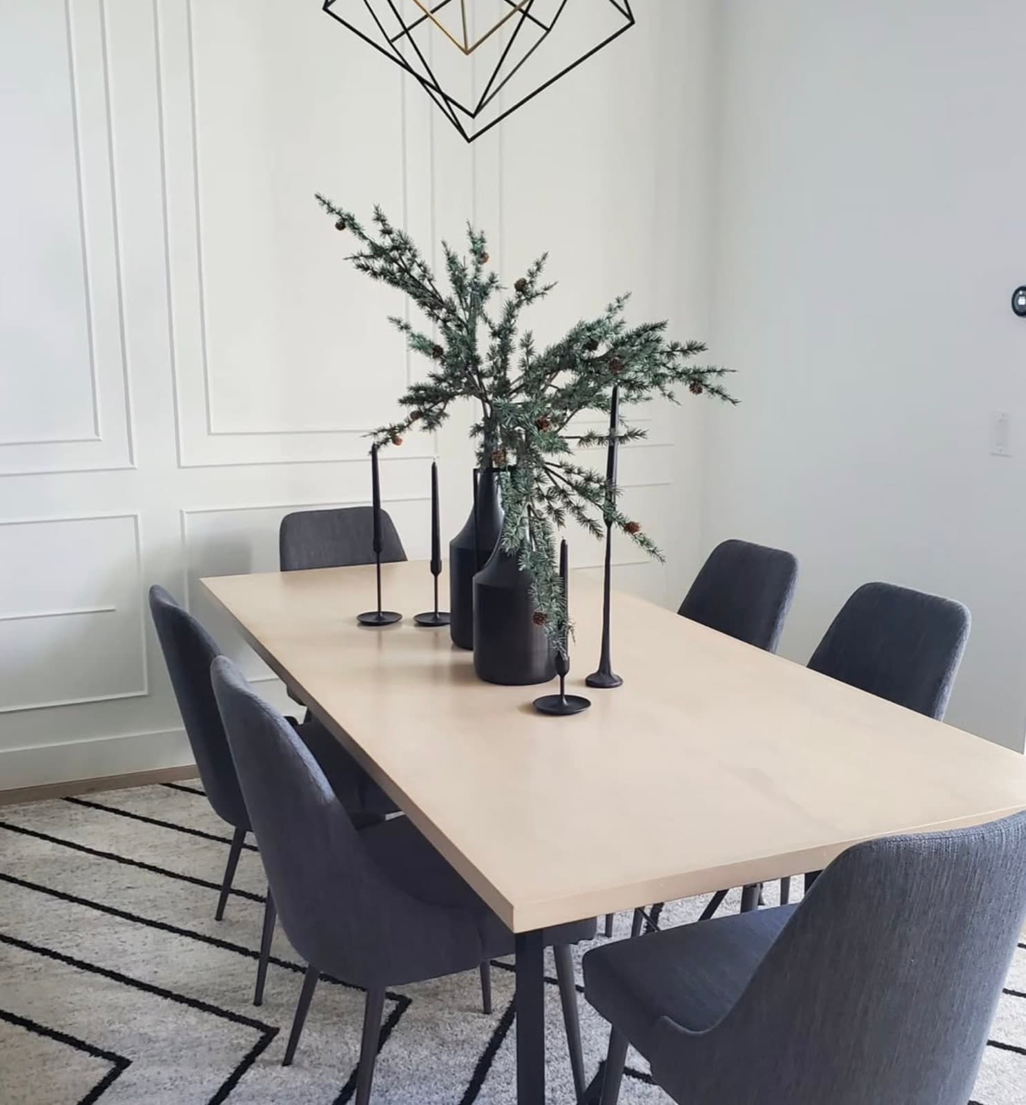 Dining table centerpiece of evergreen branches in black vases with taper candles