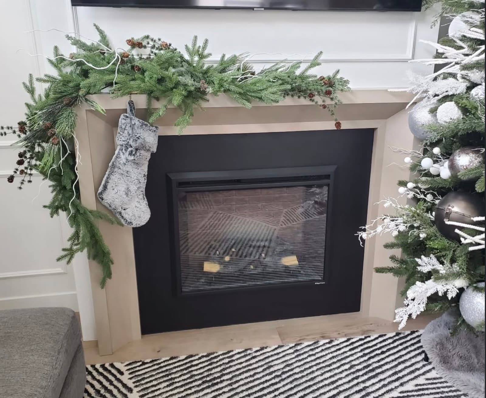 Fireplace mantel draped in pine garland with pinecones and a faux fur stocking